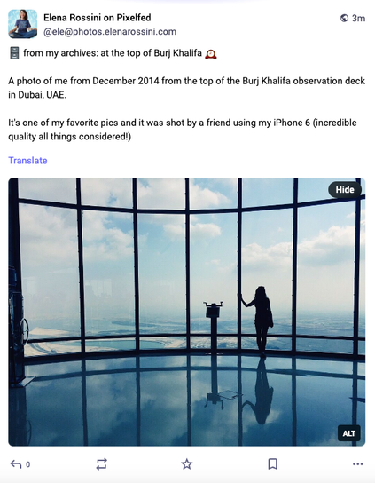 a screenshot of a photo I posted on Pixelfed. The username reads: Elena Rossini on Pixelfed and the caption states: from my archives: at the top of Burj Khalifa.

A photo of me from December 2014 from the top of the Burj Khalifa observation deck in Dubai, UAE.

It's one of my favorite pics and it was shot by a friend using my iPhone 6 (incredible quality all things considered!)

Then there is the photo of the silhouette of a woman looking out in front of her at the Dubai landscape. You can see tall large windowpanes and the whole photo is bathed in blue hues