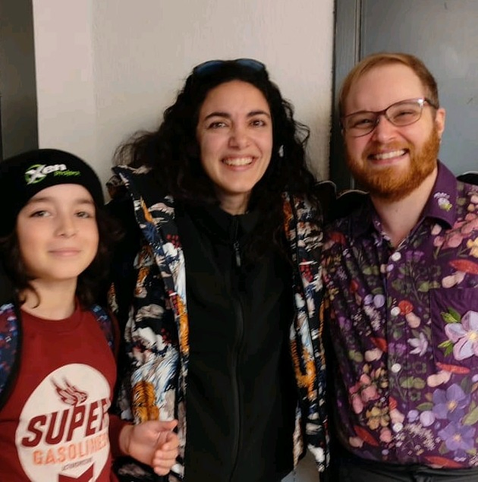 Sage stands next to their 2014 Linux Kernel intern at FOSDEM 2024. Xenia's kiddo is standing next to them. It was his first time at a free software event.