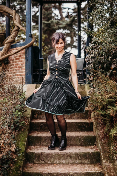 Une jeune femme brune descend les marches d'un kiosque en bois et vieilles pierres, comme abandonné dans la végétation dense. 
Elle porte un ensemble que j'ai créé, composé d'un gilet en coton noir à motifs d'étoiles vertes, et une jupe patineuse assortie. 
Elle tient sa jupe et la fait virevolter en descendant les marches. 

Modèle : Julie
Photographe : Namidaël Photographies