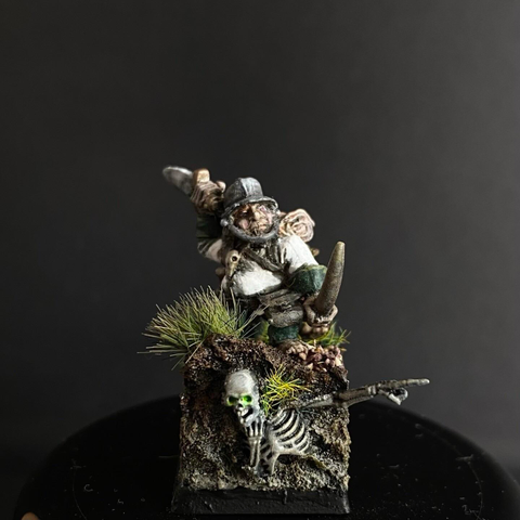 A Halfing, Rollleaf Drumlinhat, Master of the Pot on a barge of the Stir River Patrol. Halfing Cook from the Mordheim range. On a scenic base, painted in green and white livery. The base has a skeleton peering out of the base choking and pointing. My first entry in @Berit’s #FediPaint 