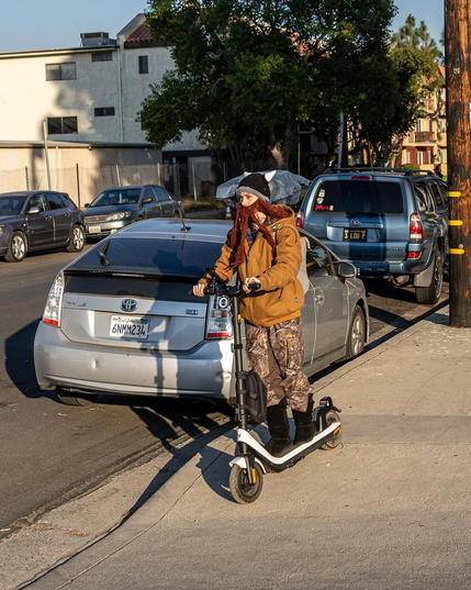 A person riding a rented scooter wearing a crocheted viking helmet with a beard attached.