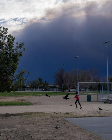 A person in exercise gear runs alongside crows. Dense smoke from the Los Angeles fires is in the background