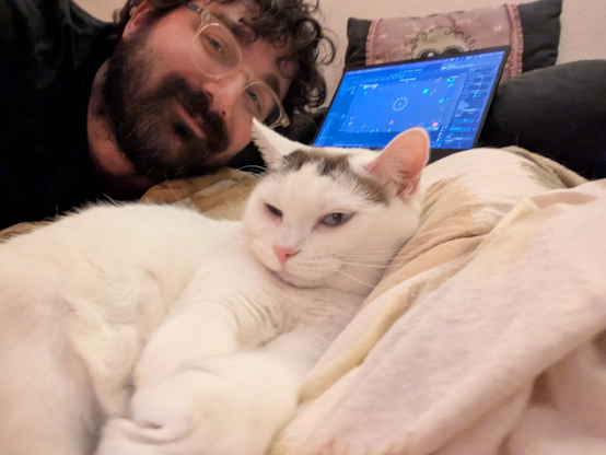 Probably, like, the only selfie I'll post here? There's my cat Boule in the foreground, extending an arm as if he's the one taking the picture.

I'm leant over him, a 30-something with glasses, a beard that I should definitely trim, and a black tee-shirt. 

There's also my laptop in the background. We see on the screen the Godot editor and a window with colorful geometry in it. That's my current project, that I let run for a few dozens of minutes to check stability