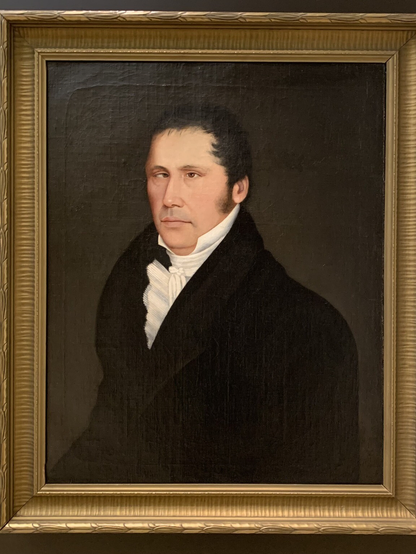 A framed portrait of a man wearing a dark coat and a white shirt, with a neutral expression, set against a dark background. Picture taken in the Musée national des beaux-arts du Québec.