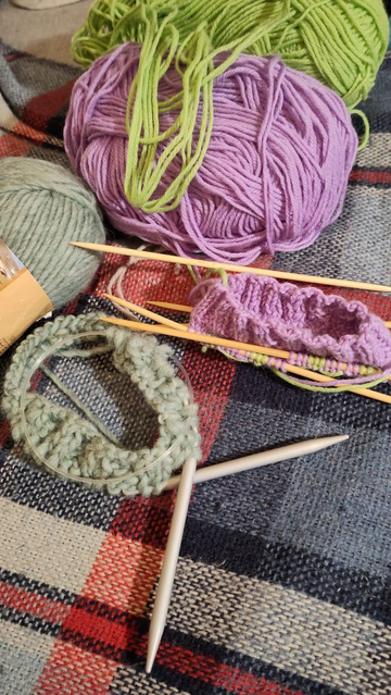 Beginnings of knitting projects, one is a thick light green yarn that's turning into a beanie, the other a beginning of a sock in bright green and purple.