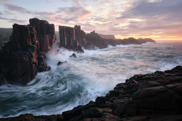 Waves crashing against rock walls on the coast at sunrise. 