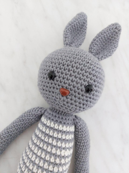 Bunny amigurumi made out of gray and white acrylic yarn, with safety eyes and nose.