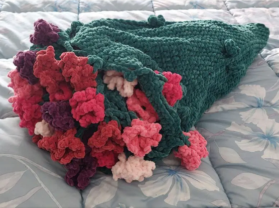 Crochet bouquet blanket, displayed in its bouquet form. It's made out of soft chenille yarn. The main piece is green and has flowers in red, purple and three shades of pink.