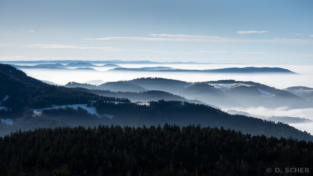 About ten successive layers of wooded hilltops separated by seas of shiny white fog trapped in the valleys under a blue sky.