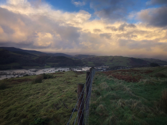 View of the Dyfi valley in Wales, showing a flooded river, hills and a cloudy sunset sky