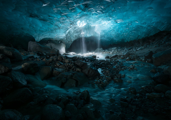 Looking towards the rear of an ice cave. Water and light are spilling through a moulin in the centre of the cave.