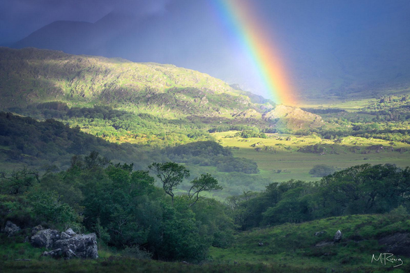 A rainbow cuts through a gloomy mountain background as sunlight breaks onto the landscape at Ladies View in Ireland