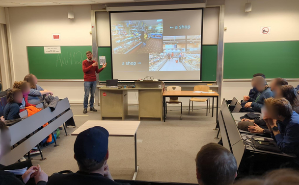 Bunch of people in a small university amphitheater room attending a talk with illustration slides.