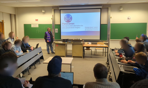 Bunch of people in a small university amphitheater room attending a talk with illustration slides. The speaker is wearing a purple Panoramax vest.