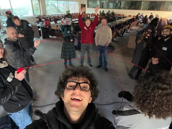 Selfie of me with a group of people standing in a circle and holding a red yarn that connects them.