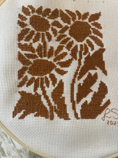 A completed cross-stitch on white Aida of brown daisies.