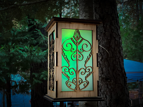 Lantern hanging in trees at dusk, green glow through a stylized oak leaf design