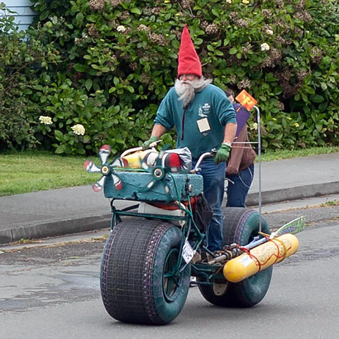 Photo of an elderly man with a long beard, wearing gardening gloves, jeans, a red pointy hat, while riding upright on a modded fatbike kitted up as if heading to a rave party in an abandoned warehouse in San Francisco