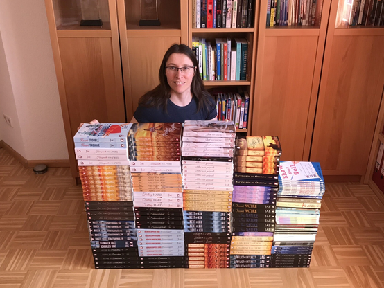 Jae kneeling behind a wall of her books, smiling