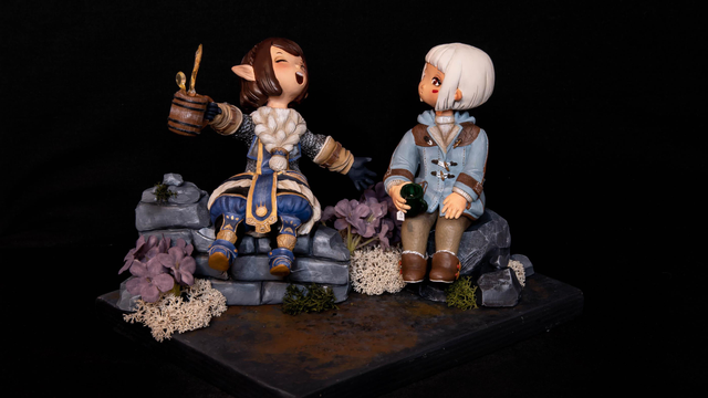 A clay sculpture (polymer clay) of the character Giott from Final Fantasy 14, and my own. Giott is a dwarf (a Lalafell, halfling) with a brown bob and armor, holding up a cup of ale that spills liquid. My character Bruni looks puzzled at her, holding a cup of tea. She's dressed in a light blue jacked and brown pants. They both sit on the remnants of a ruin wall with purple flowers (situated in Lakeland ingame).