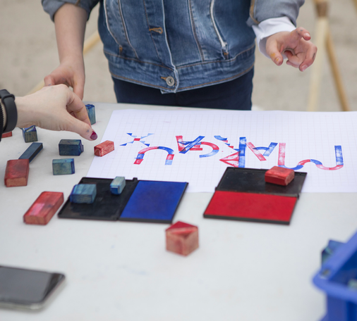 Outdoor workshop, people handling red and blue stamps to write words. Photo: Nicolas Waltefaugle