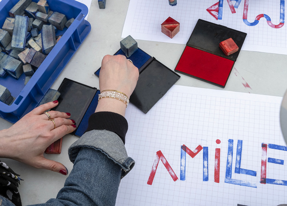 Outdoor workshop, people handling red and blue stamps to write words. Photo: Anabelle Michon