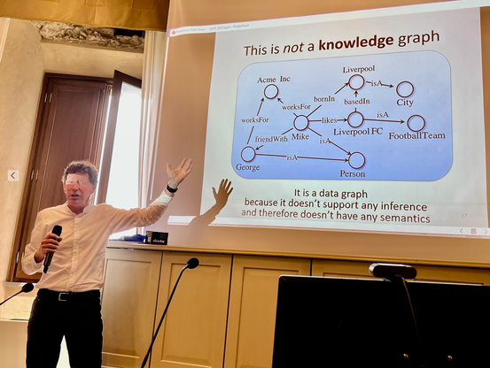 Frank van Harmelen at the ISWS 2023 presenting his keynote. The slide shown in the background has the heading "This is not a kn owledge graph". It says that the small graph depicted on it is merely a data graph as it doesn't allow for any inferencing.
