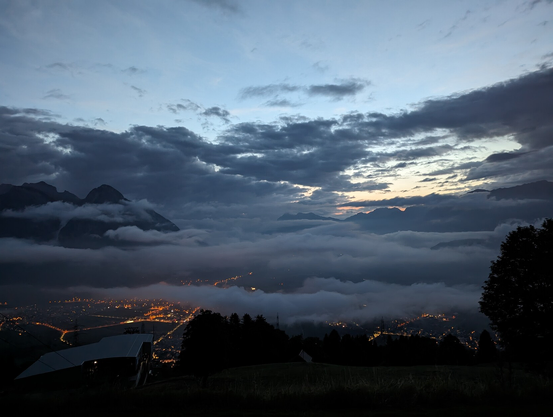 Early morning view on a Swiss valley with low hanging clouds and the lights of the town in the valley on