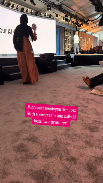 A hijabi woman shouts at a man on stage and is removed from the room