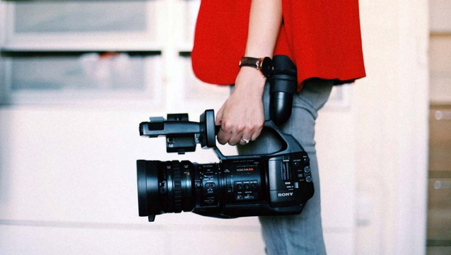 a photo of a woman - you can see her from the side, only from the knees up to her waist - wearing a bright red cape and holding a Sony camcorder in her hands