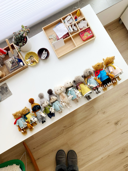 A collection of hand-stitched mohair fabric  animals, fully dressed in boys or girls outfits (including costs and across body bags + with tiny needle felted animal toy companions) in two sizes (smaller 12-13 cm and slightly larger 16-17,5 cm), arranged in a row on my work table: foxes, dogs and an elephant. 