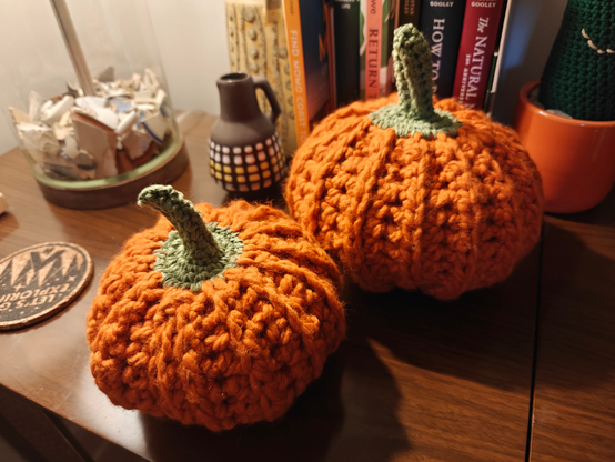 Two orange crocheted pumpkins on a shelf