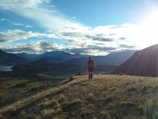 An incredibly handsome (yet modest) man strides away from the camera across a hilltop bathed in late evening sunshine.