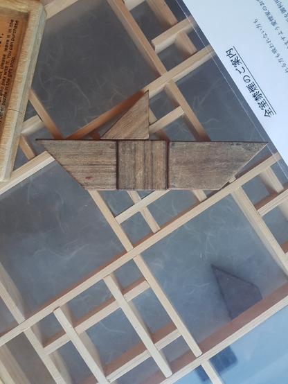 Wooden puzzle assembled in a symmetrical boat-like shape with flat bottom and two triangular sails, placed on a glass surface.