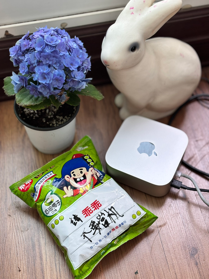 나무 바닥 위에 Mac mini가 놓여 있고, 그 옆에 臺灣 菓子인 草綠色 封套의 乖乖가 놓여 있다. 乖乖에는 「請〈乖乖〉，不要當機」(말 잘 듣고, 다운되지 말아라)라고 써져 있다. 주위에는 흰 토끼 某樣 電球와 파란 꽃이 든 花盆이 있다.