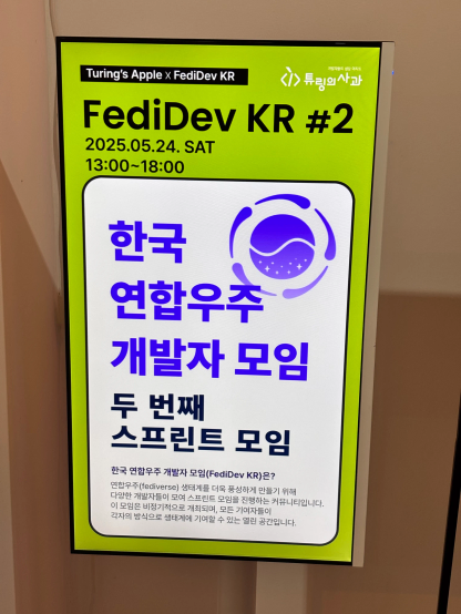 튜링의 사과 입구 앞에 위치한 TV 화면에 한국 연합우주 개발자 모임(FediDev KR) 두 번째 스프린트 모임의 배너가 표시되어 있다.
