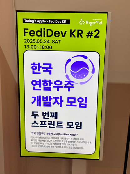 A bright green poster for FediDev KR #2 sprint event, showing the date 2025-05-24 Sat 13:00–18:00. The poster features Korean text announcing a FediDev KR sprint session, with the Turing's Apple logo and a circular blue logo with wave-like design. The poster is displayed on a TV at the entrance of the venue.