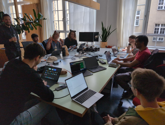 Photo of 10 hackers at a table in the 101lab office in Berlin, working on their laptops.