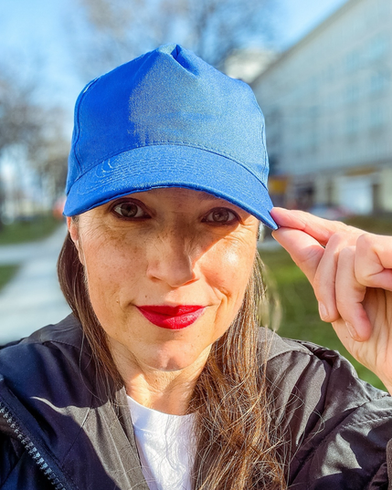 Selfie von Sophie mit blauem Basecap auf dem Kopf. Sie trägt roten Lippenstift und lächelt in die Kamera.