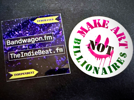 Two stickers. One is square and shows the URLs Bandwagon.fm and TheIndieBeat.fm on a sparkly blue background. The other is round and graffiti style with the words Make Art Not Billionaires in pink and black on a white background. They will look cool on your laptop, notepad, car, water bottle, guitar, violin, flute, or battle axe!