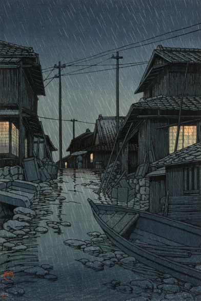 Rain falls on a narrow lane in a town by the seaside in Kawarago, Miyagi Prefecture. In the foreground, a small wooden boat is pulled up, lying at an awkward angle on the uneven, stony ground. Beyond, warm lights glow in the windows of houses on either side of a meandering little lane; up ahead, a single pedestrian carrying an umbrella passes beneath wires strung between utility poles. Rain continues to fall across the scene; the ground is slick with rainwater, and the sky above is dark and overcast.