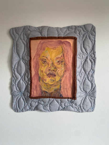 A painting of a portrait of woman looking straight ahead in pink and yellow hues. The painting has a light blue quilted frame