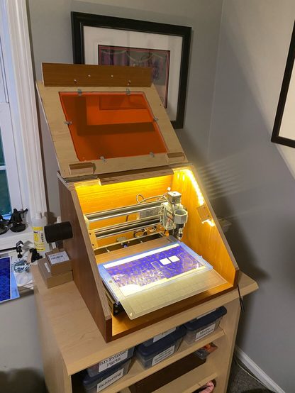 The angled enclosure is open and the CNC machine in more clearly visible. LED lighting is visible around the interior and the bed of the machine has a layer of bright purple vinyl attached.
