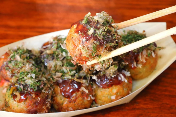 A plate of takoyaki with one being picked up by chopsticks