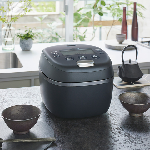 An onyx-colored Tiger rice cooker on a nice dark marble countertop with a bowl on each side