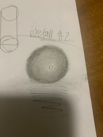 Pencil sketch on white paper titled "eyeball #2," showing a shaded circle resembling an eyeball with a rough texture, plus a cylinder.