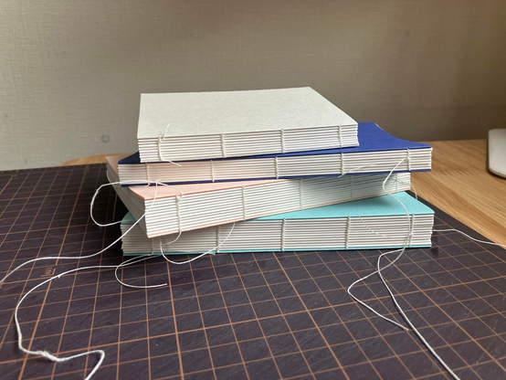 糸かがり製本の手製本ノート（仕上げ前）を4冊重ねて、背のかがり糸が見えるように撮った画像
