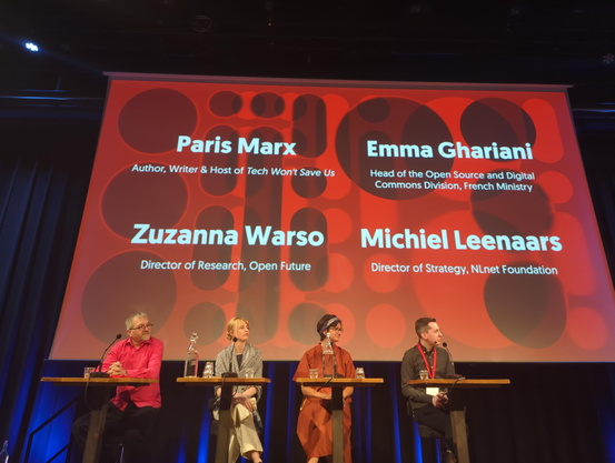 On stage in front of a slide with the names:
Paris Marx, Author, Writer & Host of Tech Won't Save Us 

Emma Ghariani Head of the Open Source and Digital Commons Division, French Ministry

Zuzanna Warso,  Director of Research, Open Future Director of Strategy

Michiel Leenaars, NLnet Foundation