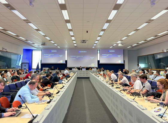 Conference room, participants listening, mastodon presenting with slides in the background