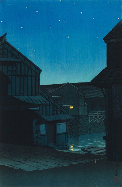 Evening on the banks of Nagoya's Hori River. In the foreground, a single small wooden boat is pulled up on a sloping launch; the water of the river is still. Warehouses crowd close together on the canal bank, their doors shut, windows dark and shuttered - except for one light glowing in a single window, reflected in the water below. Above, stars shine in the cloudless night sky.